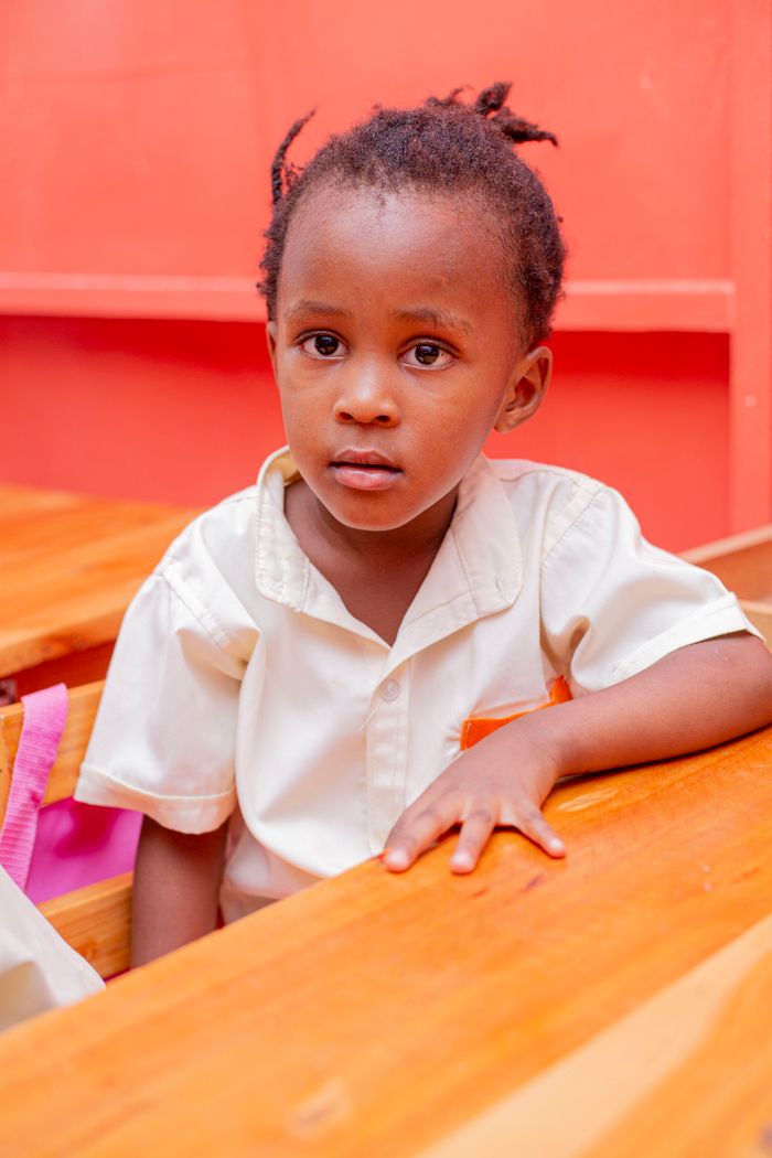 A young child in a school uniform sitting at a wooden desk in a classroom setting.