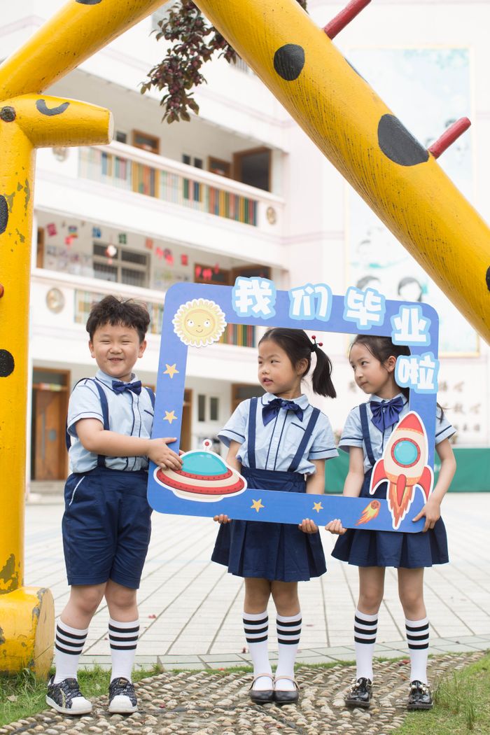 Three children holding a graduation frame outdoors, symbolizing joy and achievement.